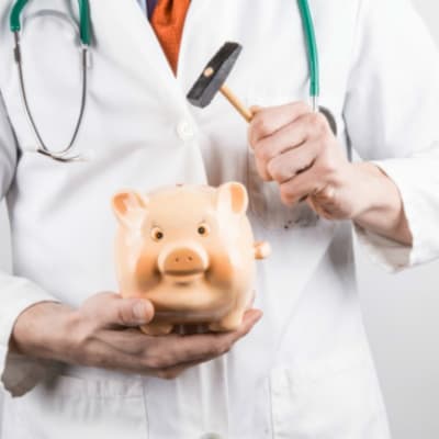 En doktor håller i en spargris och en hammare, redo att slå sönder spargrisen