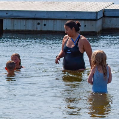 Barn och simskollärare i vattnet invid en brygga.