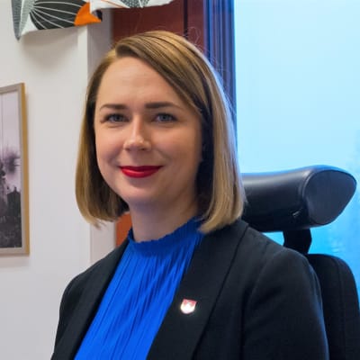 Miira Raiskila istuu työhuoneessaan ja hymyilee. 