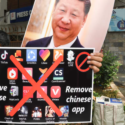 Mielenosoittaja pitää kiinalaisia sovelluksia vastustavaa kylttiä ja Kiinan presidentin kuvaa