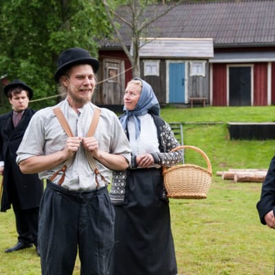 två skådespelare står i gamla kläder med rynkande miner och lyssnar på en gammaldagsklädd präst i pjäsen frihetsdrömmar