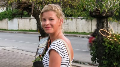 Sara promenerar på trottoaren och vänder sig leende mot kameran.