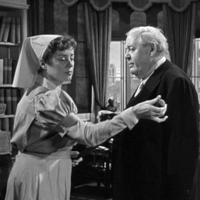 Sairaanhoitaja (Elsa Lanchester) ruuvaa irti kävelykepin nuppia. Asianajaja Sir Wilfrid (Charles Laughton) katselee harmistuneena. Taustalla sihteeri (Ian Wolfe). Kuva elokuvasta Todistaja (Witness for the Prosecution)