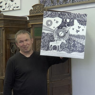 Taiteilija Juri Lisovski esittelee teostaan ateljeessaan. Sen yläosassa henkilö istuu karhun selässä, aurinko paistaa ja linnut lentävät. Alaosassa mies istuu hirven selässä, taivas on tumma ja kuu paistaa. Kuvan osat ovat ikään kuin toisilleen vastakkaiset.