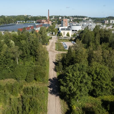 Kaupungin viheralueiden läpi kulkee hiekkatie, jonka päässä on teollisuusrakennuksia.