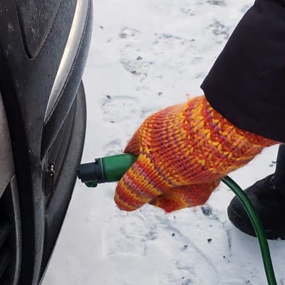 En person lägger in en motorvärmarsladd i en bil vintertid.