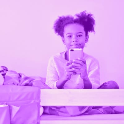 Lapsi istuu sängyssään puhelin kädessä.