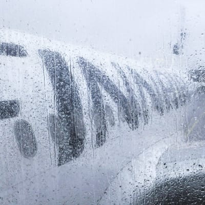 Regndroppar mot ett fönster. Man ser ett Finnair-flygplan från fönstret.