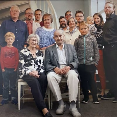 Ragnar och Brita sitter bredvid varandra omgivna av alla sina barn, barnbarn och barnbarnsbarn. 