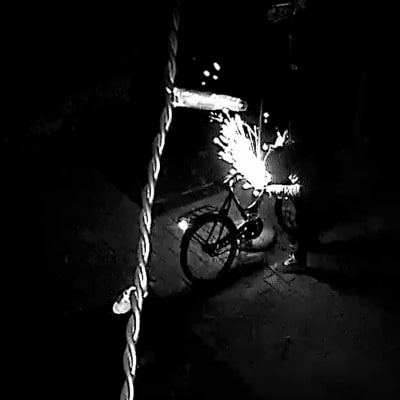 En tjuv söndrar ett cykellås med en batteridriven vinkelslip på natten.