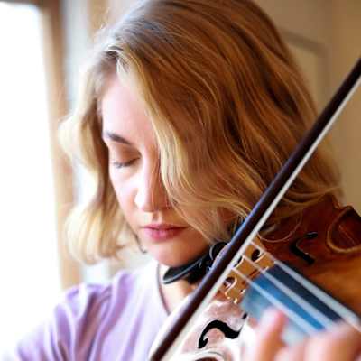 Nainen soittaa viulua luonnonvalossa ikkunan äärellä silmät kiinni.