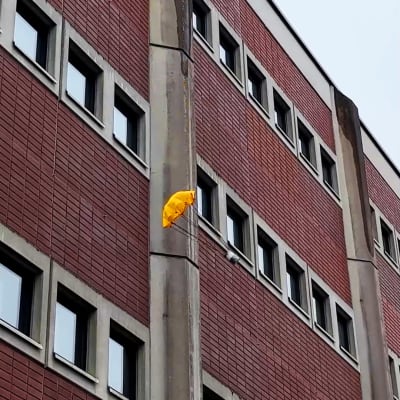 En burk fastspänd i en liten fallskärm singlar ner mot marken framför en tegelvägg.
