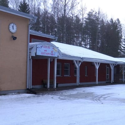Skolbyggnad med röd fasad. På väggen hänger en klocka.