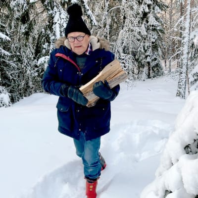 Mies kantaa polttopuita lumisessa maastossa.