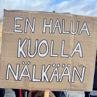Människor demonstrerar i bakgrunden och håller upp en skylt där det står "jag vill inte dö av hunger". I förgrunden en inklippt svartvit bild av Anna Back.