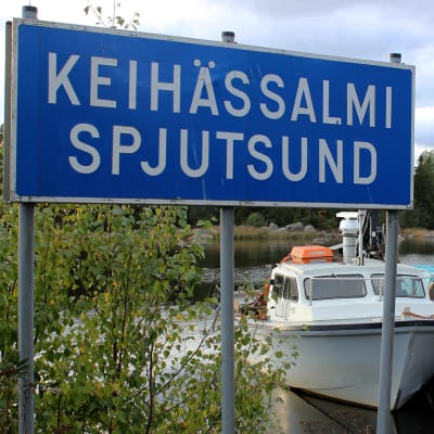 Kyltti, jossa lukee Keihässalmi, Spjutsund. Taustalla vene.