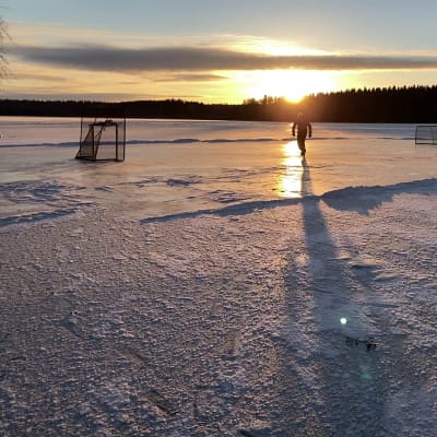 Mies luistelee järven jäällä auringon laskiessa.