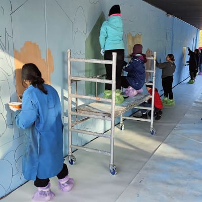 Nuoret maalaavat seinämaalausta rakennuksen seinään.