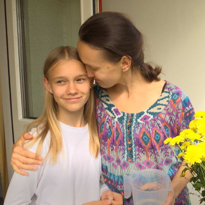 Yuliia Charkina och hennes dotter omfamnar varandra på en balkong med gula blommor. 
