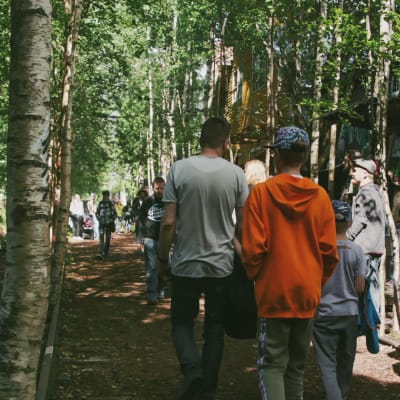 Människor promenerar på festivalområde mellan träd och en vägg med graffitimålningar.