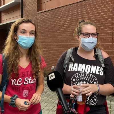 Tre personer med munskydd på står framför en röd tegelvägg vid ett förhandsröstningsställe i North Carolina.