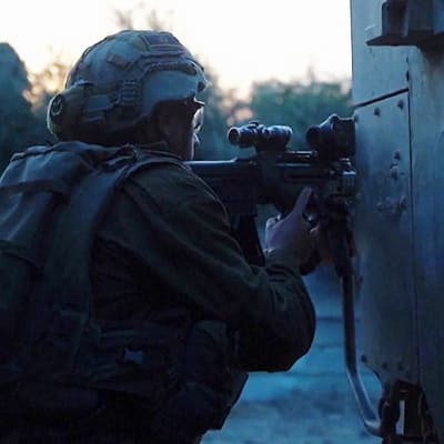 Israelin sotilas väijyy hämärässä tankin takana.