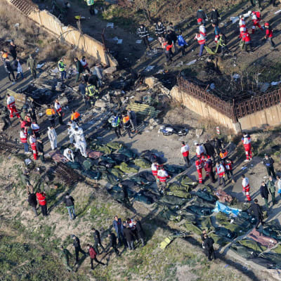 Bild uppifrån av olycksplatsen i Iran där ett Ukraine International-plan störtat. Räddningsarbetare går omkring och likpåsar ligger på rad.