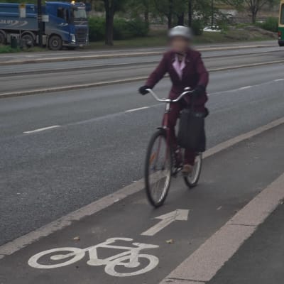 En kvinna kör med en cykel på ett enkelriktat cykelfält i fel riktning. I bakgrunden syns en spårvagn.