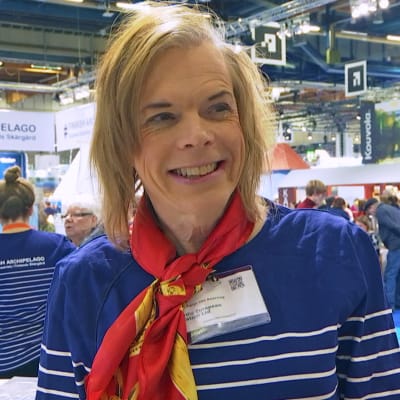 Tanja von Knorring på resemässa med en scarf runt halsen och leende tittande förbi kameran. 