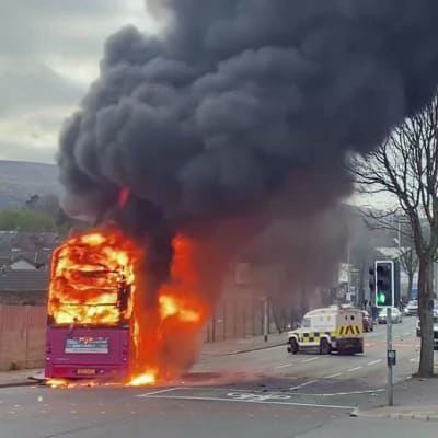 En röd tvåvåningsbuss brinner på en gata.
