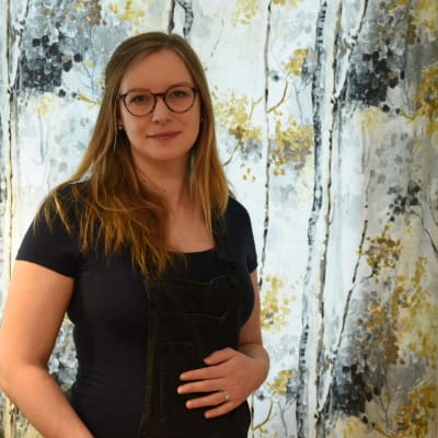 Victoria Hartman tittar in i kameran och håller handen på sin gravida mage