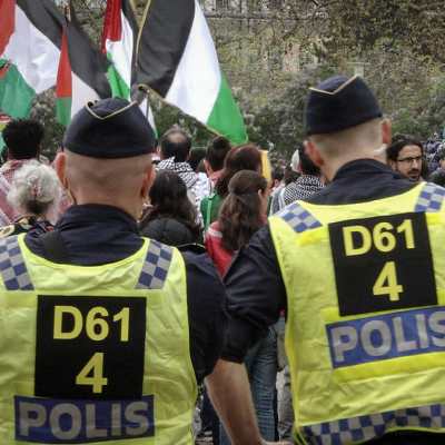 Två poliser tittar på en demonstration med palestinska flaggor.