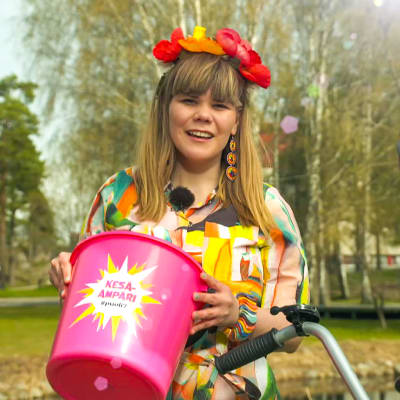 Toimittaja Ruut Parikka kesäisissä vaatteissa kädessään pinkki ämpäri, jossa lukee Kesä-ämpäri.