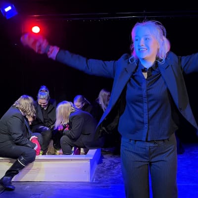 Nainen nostaa kädet ilmaan voittajan elkein teatterin näyttämöllä.