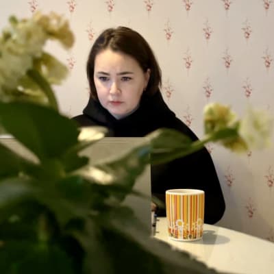 Tummahiuksinen nainen katsoo keskittyneesti tietokoneen näyttöä.