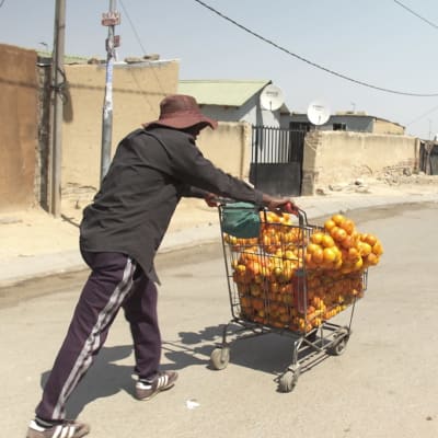 Hattupäinen katukauppias työntää appelsiineja kaupan ostoskärryssä köyhän asuinalueen kadulla Etelä-Afrikassa