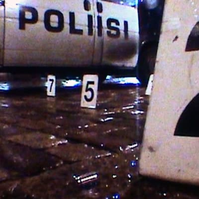 Poliisin asettamia numerokylttejä kadulla, taustalla poliisiauto.
