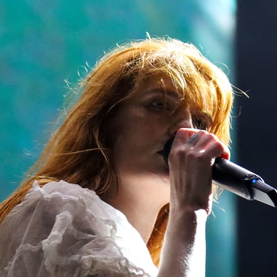 Florence + the Machinen solisti Florence Welch kasvot Flow-festivaalin lavalla. Laulaja laulaa ja pitää mikrofonia suunsa edessä. 