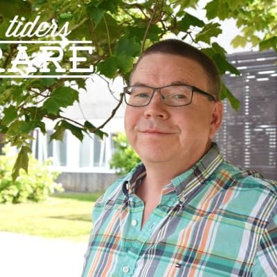 Man står i skuggan under ett träd. I bakgrunden är ett hus.