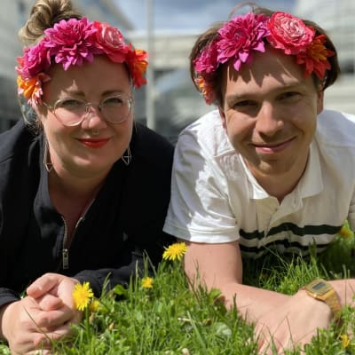 Programledarna för Hangö Teaterträff 2020 Kia Svaetichin och Tom Rejström ligger på gräsmattan med blommor i håret