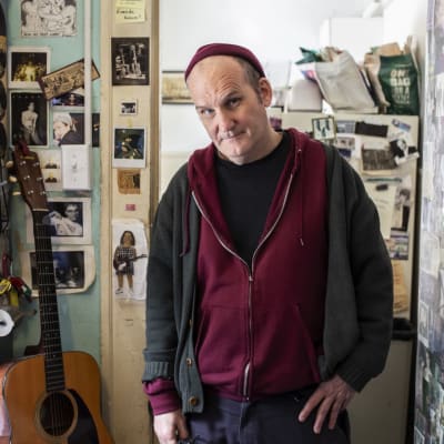 Yhdysvaltalainen muusikko Ian MacKaye Dischord House -nimisen talon oven suulla. Seinillä ja ovessa kymmeniä punk-bändien kuvia. 