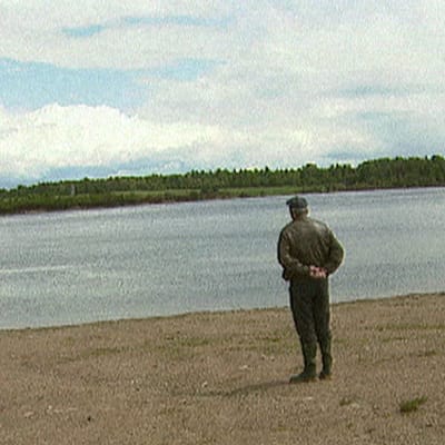 Jakaväkirykmentti 12 sotaveteraani katselee tunteikkaana järven rannalla yli veden. Selin kameraan.