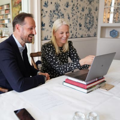 Kronprinsen och kronprinsessan i Norge deltar i videosamtal med en laptop framför sig.