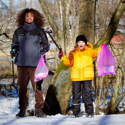 Yle Galaxin Saku ja Lumi hymyilevät keväisessä metsässä kädessään roskapussit ja roskapihdit.