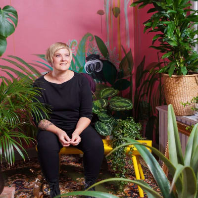 En kvinna sitter i ett rum med många grönväxter.