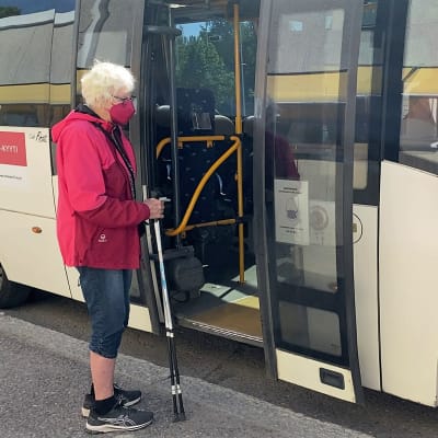 Vanhempi nainen kävelykeppien kanssa on nousemassa minibussiin.
