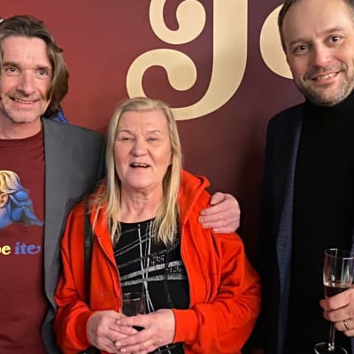 Mika Räinä, Ulla Ruonansuu ja Marko Talli seisovat Jope ite-elokuvan banderollin edessä.