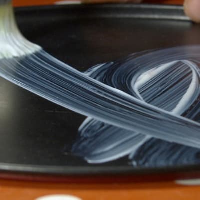 Närbild av pensel med lim på kakformsbotten.