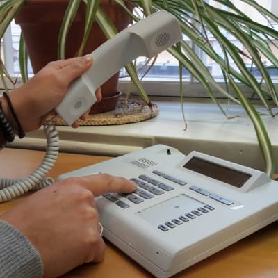 En hand lyfter telefonluren och ett nummer trycks.