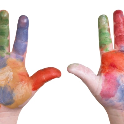 ett dagisbarns händer uppe i luften, täckta av olika färger